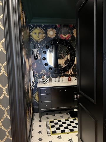 Powder room vanity view with round mirror, celestial wallpaper, and black cabinetry