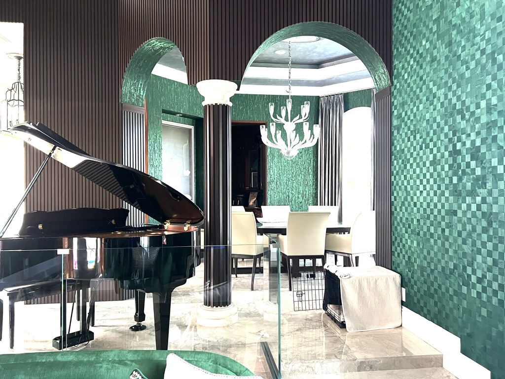 Music room with grand piano, green wall finish, fluted dark millwork, and arched opening