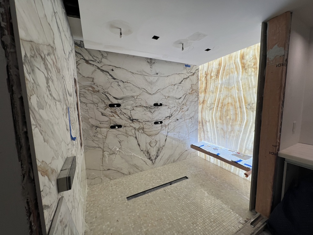 Custom shower installation with bookmatched stone slab walls and illuminated translucent stone feature