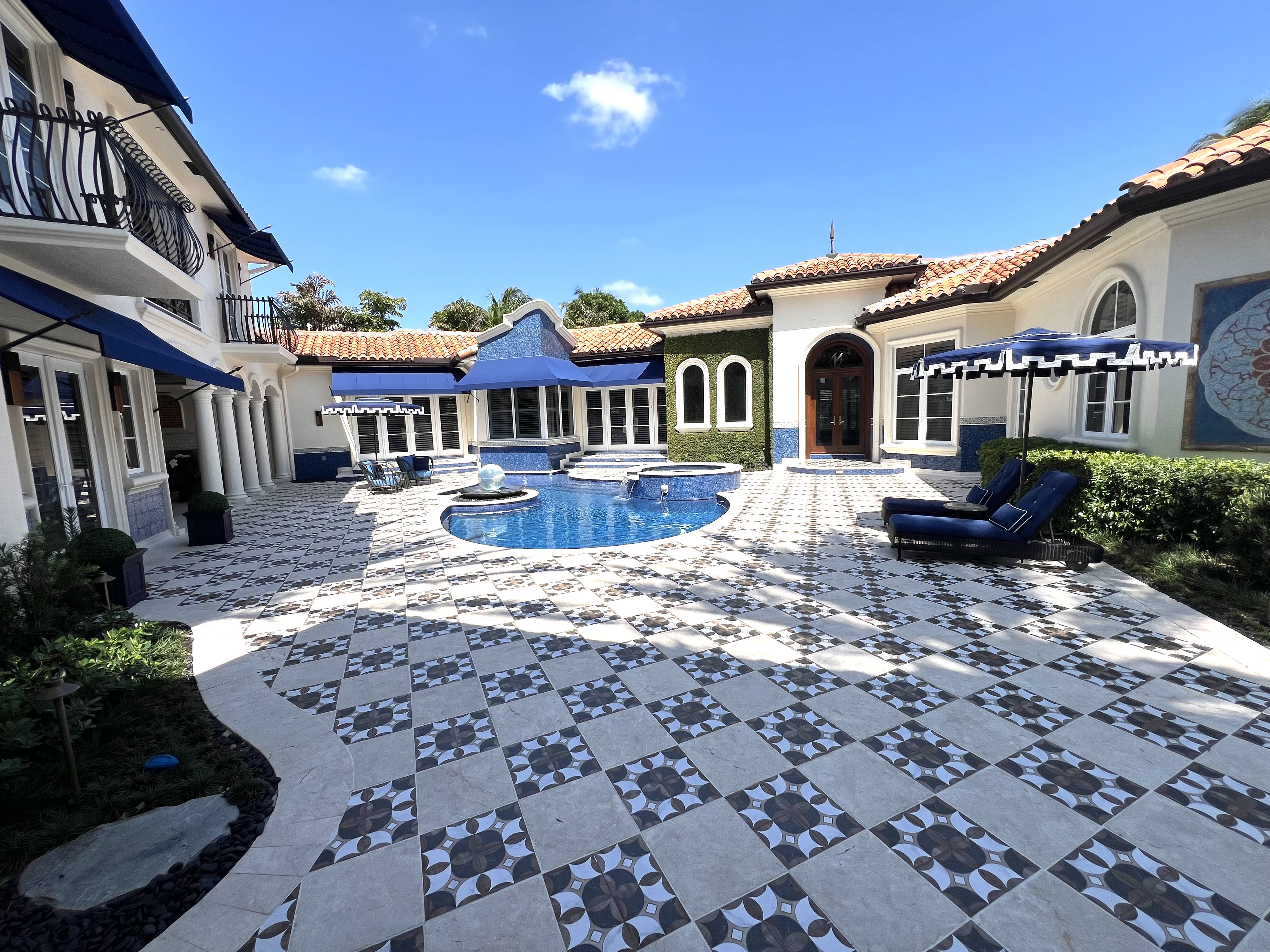Courtyard pool with patterned paving, blue awnings, and Mediterranean exterior architecture
