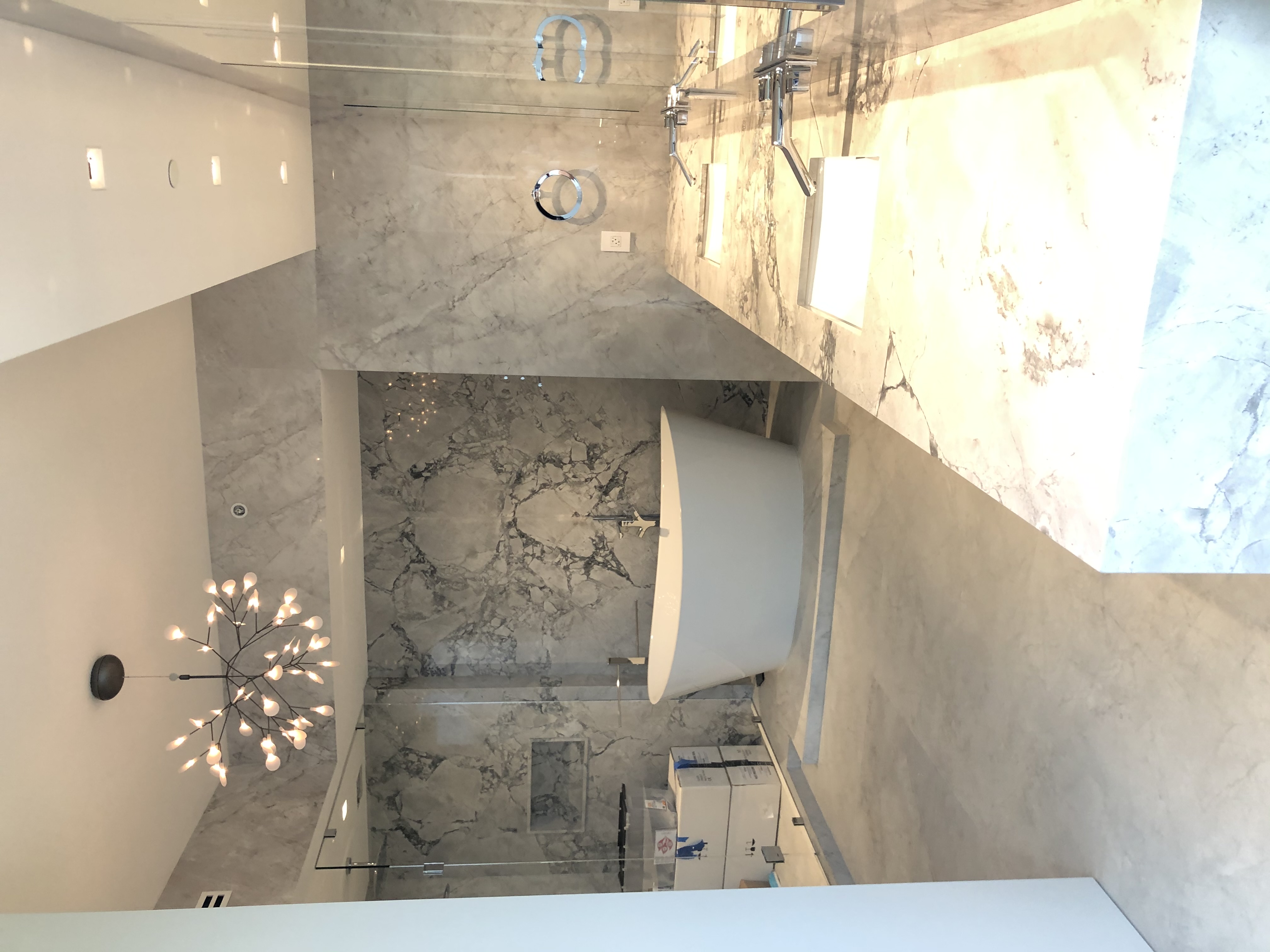 Primary bath with freestanding tub, bookmatched marble walls, double vanity, and sculptural chandelier