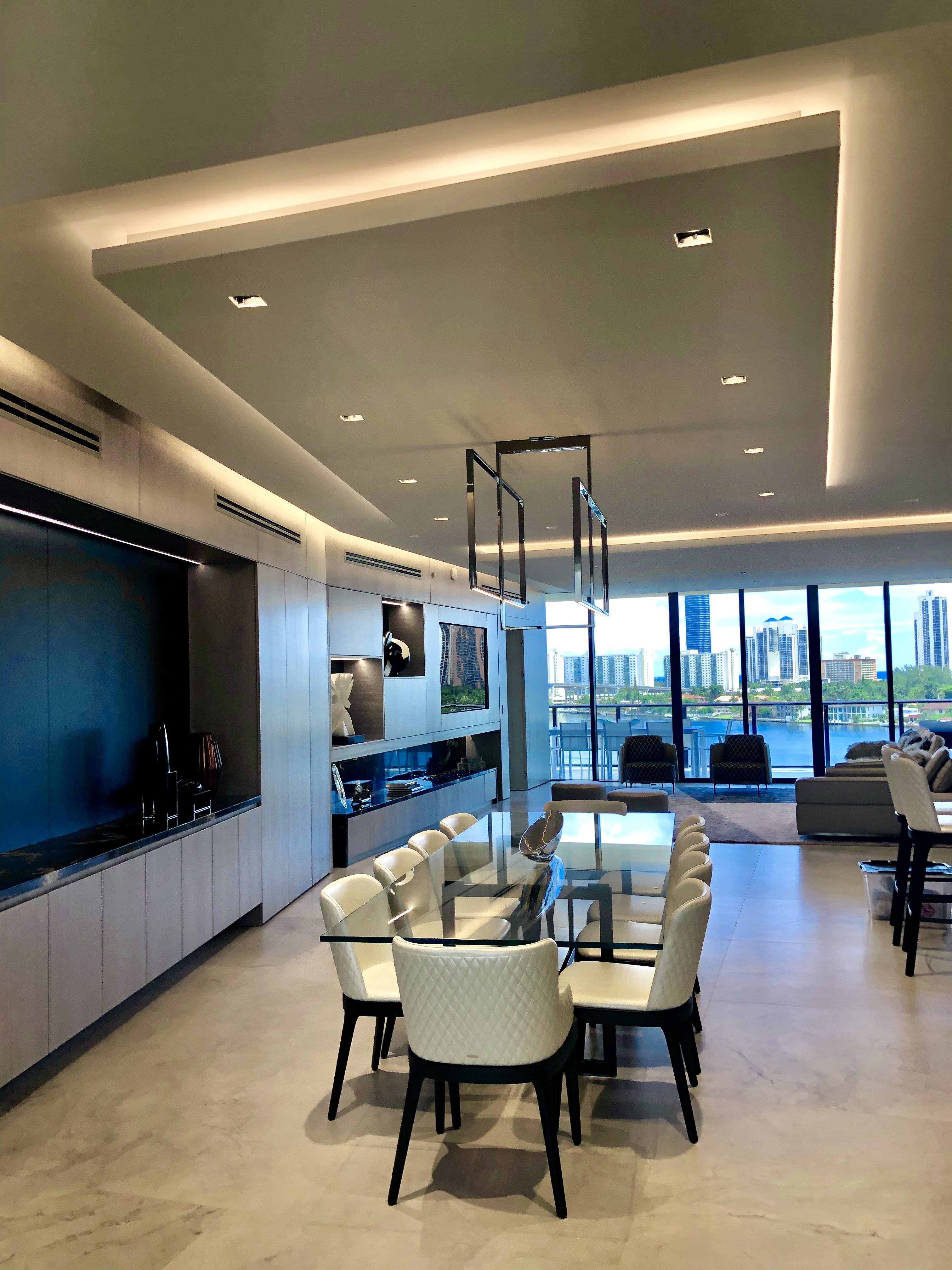 Modern penthouse dining area with linear pendant lighting and waterfront backdrop
