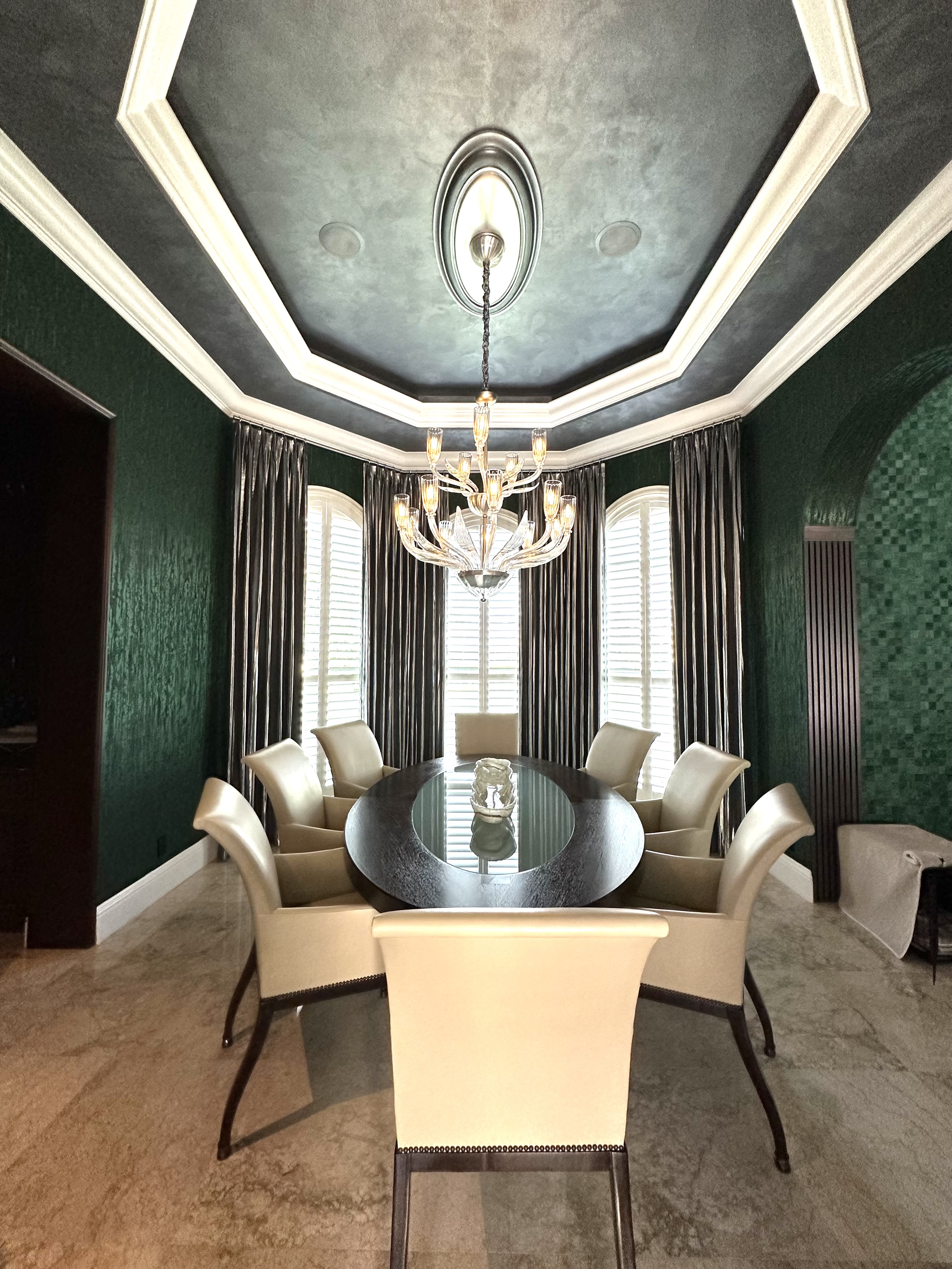 Formal dining room with deep green walls, elongated black table, and sculptural chandelier