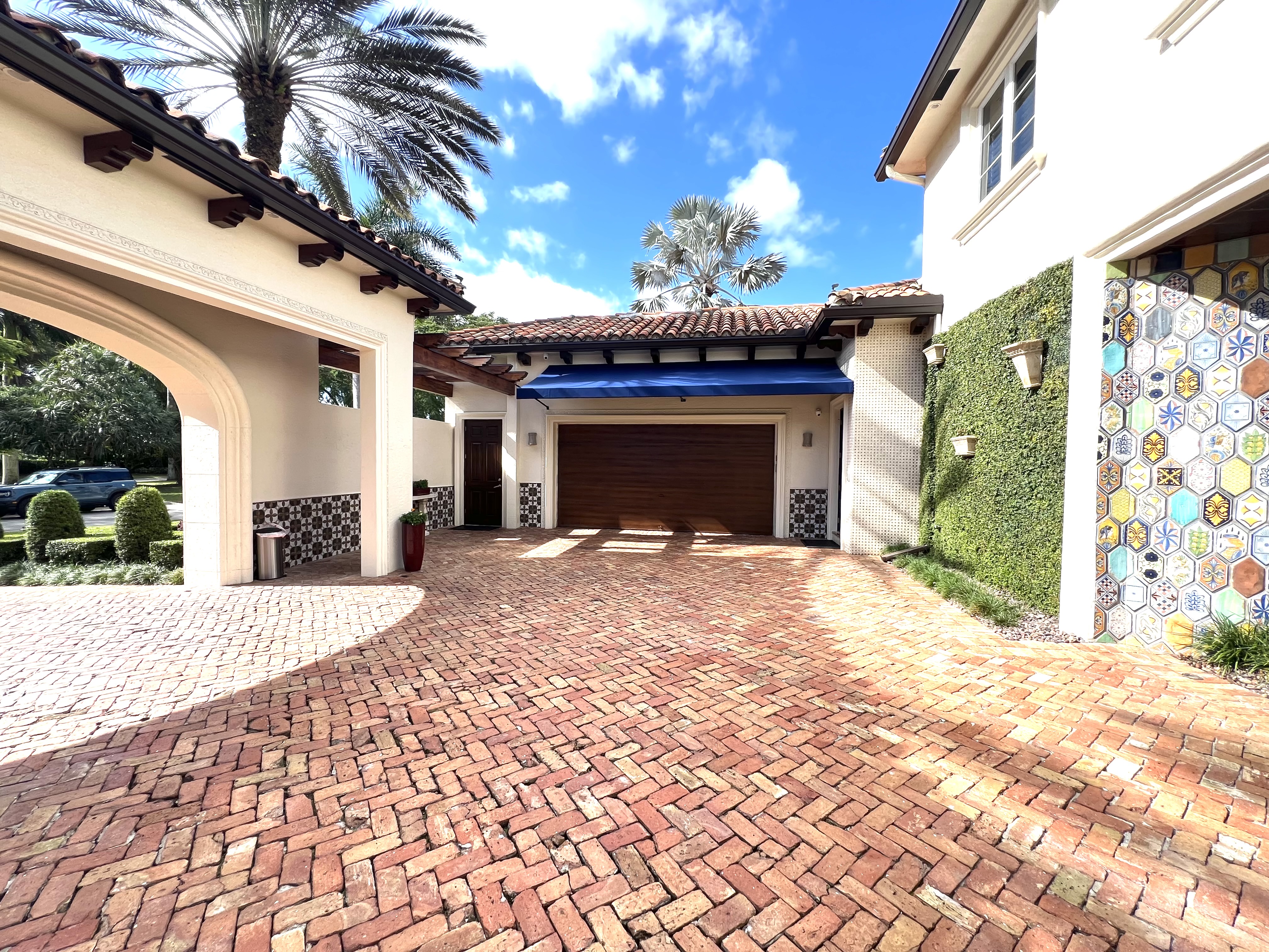 Brick motor court with wood garage door, blue awning, and decorative tile detailing