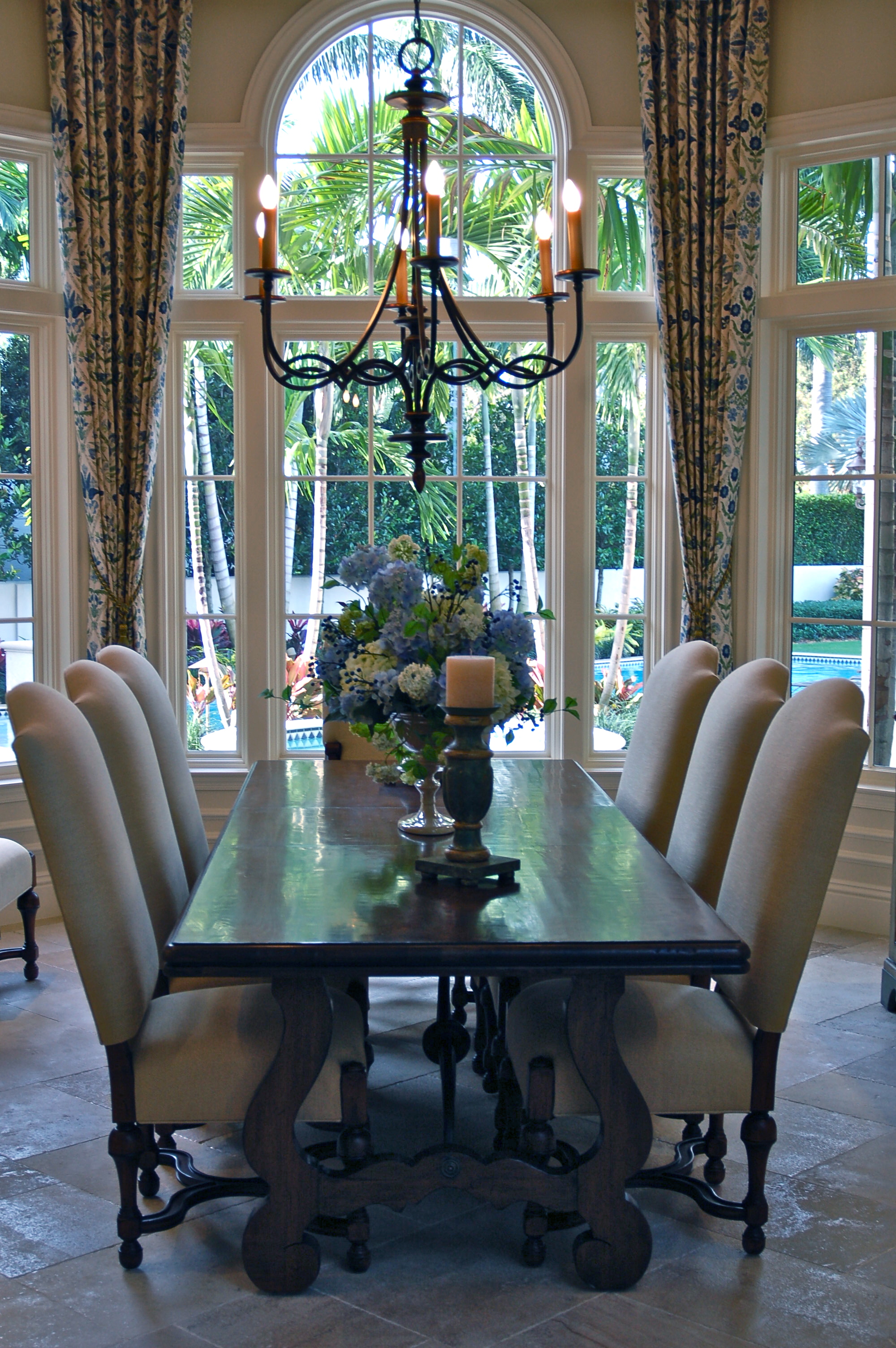Formal dining room with tall arched window, chandelier, and upholstered chairs