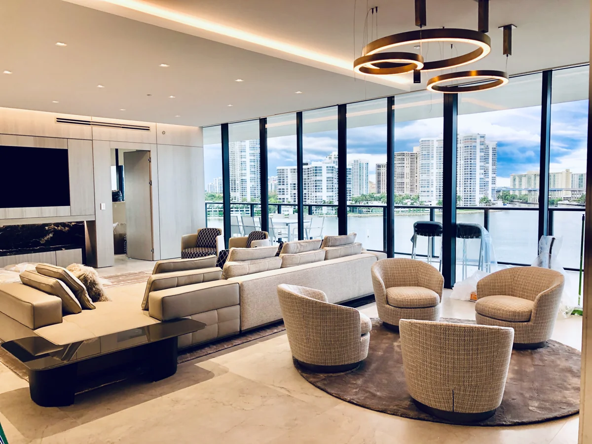 Modern waterfront living room with sculptural seating, circular pendants, and panoramic views